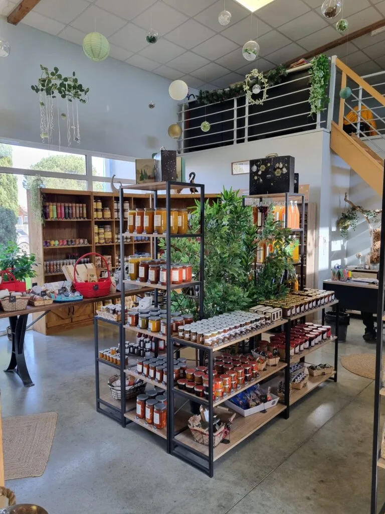 Intérieur d'un magasin avec des étagères contenant des pots de confiture et d'autres produits, des plantes décoratives et une ambiance accueillante.